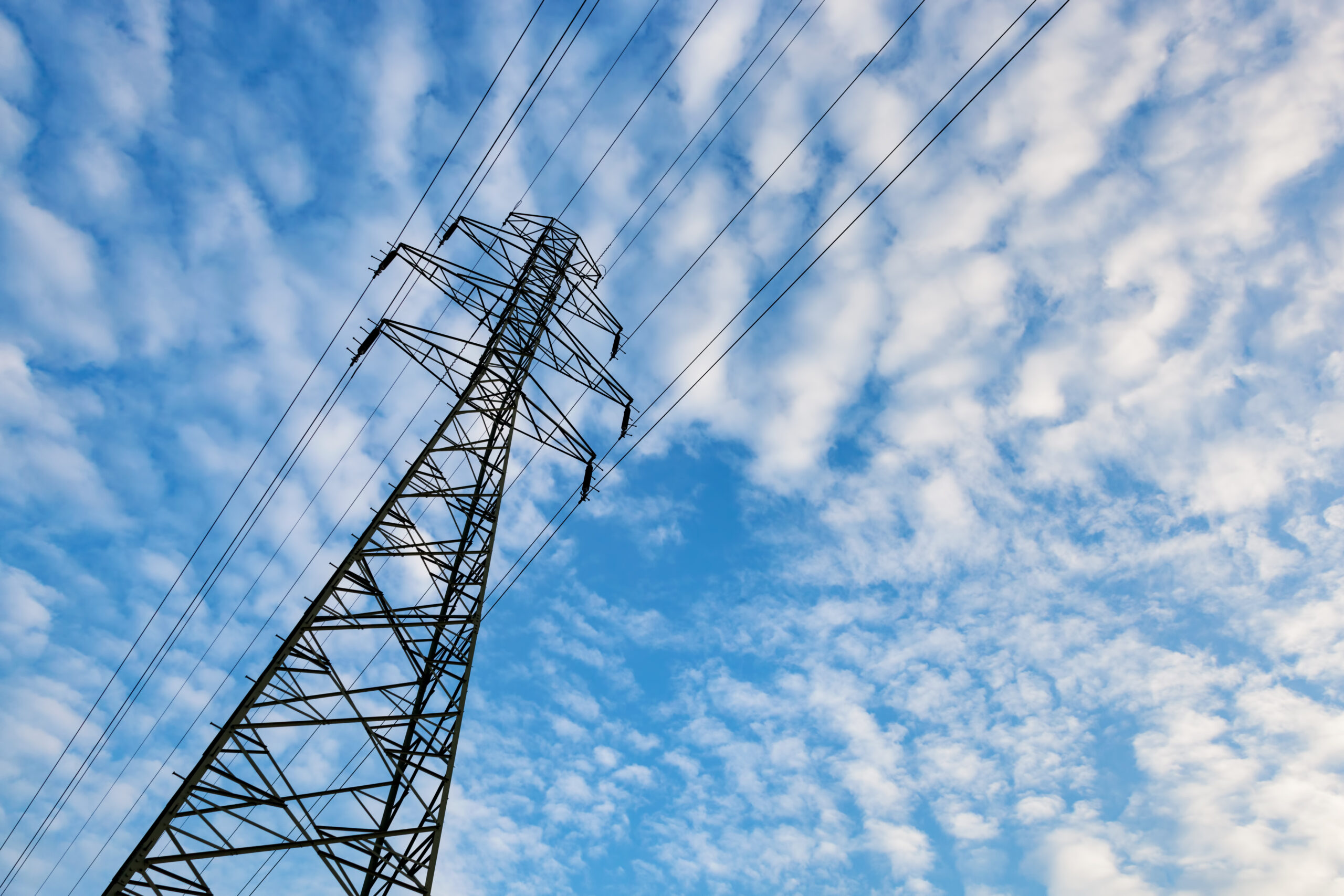 Electricity transmission pylon against blue sky with fluffy clouds